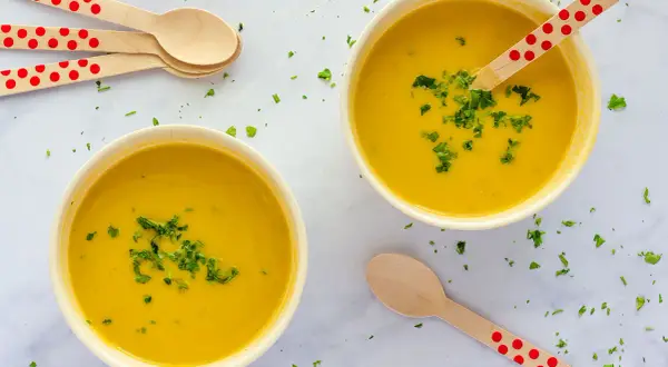 Dos cuencos de cremoso pure de verduras, decorados con perejil picado y cucharas de madera con lunares rojos.
