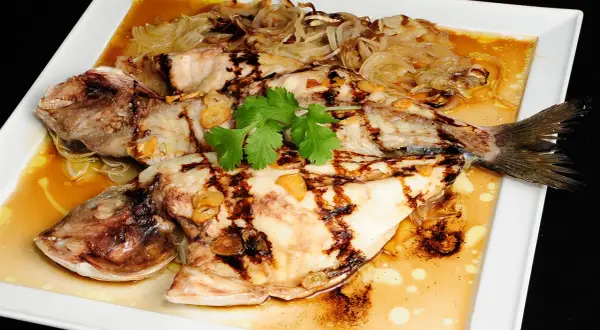 Dorada a la espalda, jugosa y a la parrilla, servida con cebolla caramelizada, ajo y cilantro fresco en una salsa dorada.