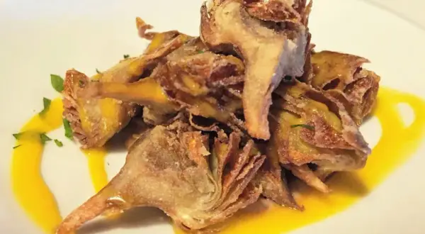 Deliciosas alcachofas fritas crujientes, servidas con una salsa dorada y perejil picado.