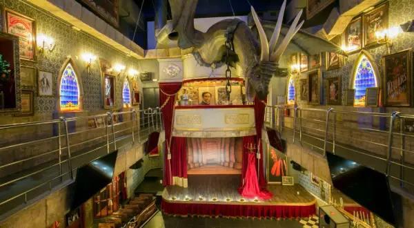 Dragón suspendido sobre un escenario teatral en el magic museum Peñíscola. Ventanas góticas y pósters de ilusionismo adornan las paredes.