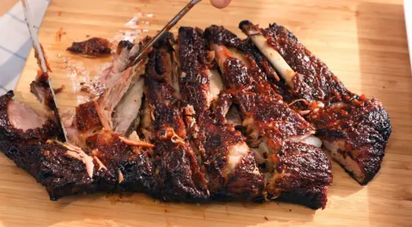 Costillas a la barbacoa jugosas y tiernas, cortadas en una tabla de madera. La carne se desprende del hueso, cubierta de salsa.