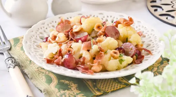 Deliciosa ensalada de coliflor con uvas rojas, prosciutto crujiente y avellanas tostadas. Un plato fresco y lleno de sabor.