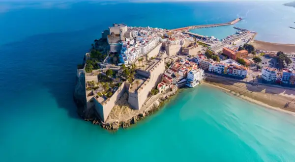 Castellón Costa Azahar: un pueblo amurallado con un castillo se alza sobre el mar turquesa, con un puerto deportivo y playas doradas.