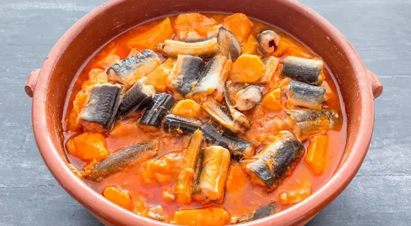 Un cuenco de barro con un delicioso all i pebre, un guiso tradicional de anguilas y patatas en salsa roja.