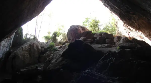 Salida de la cueva negra Montanejos, con rocas y vegetación iluminadas por el sol.