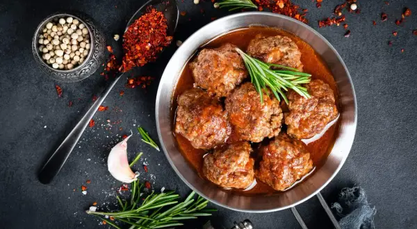 Sabrosas albóndigas con tomate, servidas en sartén, con romero, ajo y especias.
