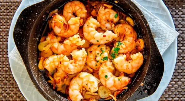 Deliciosos langostinos al ajillo burbujeando en aceite de oliva, con trozos de ajo y perejil fresco. ¡Un plato que huele a gloria!