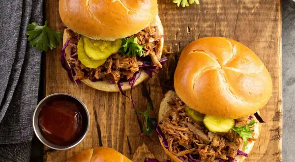 Dos jugosos sándwiches de pulled pork con pepinillos y col morada sobre pan rústico, listos para disfrutar.