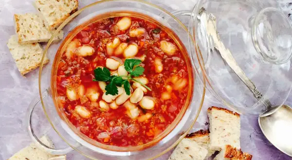 Un tazón de alubias con verduras, servido con pan rústico.