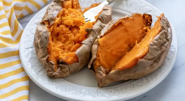 Dos mitades de boniato cocinado en freidora de aire, servidas en un plato blanco con un tenedor.