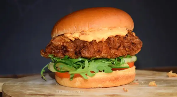 Deliciosa hamburguesa de pollo crujiente con lechuga, tomate y pepino, cubierta con una cremosa salsa.