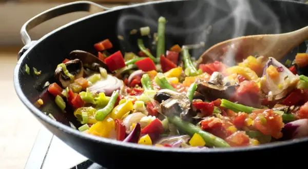 Un delicioso salteado de verduras humeante en un wok, con pimientos, judías verdes, champiñones y cebolla morada.