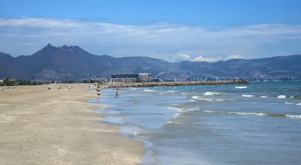 La playa del Serradal, con sus montañas al fondo, invita a pasear por la orilla mientras las olas acarician la arena dorada.