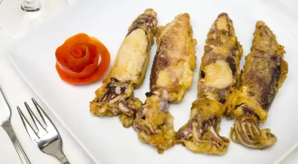 Cuatro chipirones fritos dorados y crujientes, servidos en un plato blanco con una rosa de tomate y cubiertos.