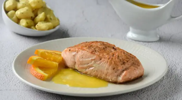 Filete de salmón a la naranja, servido con gajos de naranja y una salsa dorada. Acompaña unas patatas.