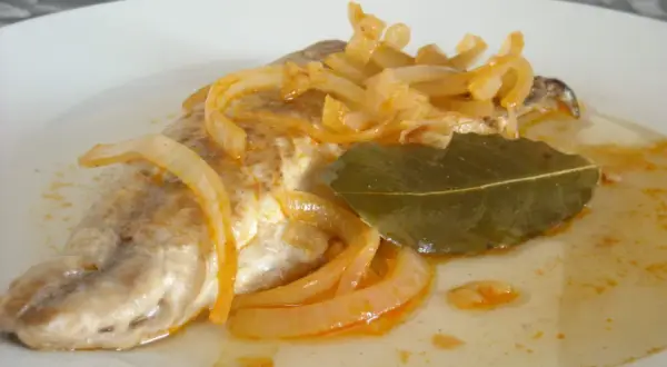 Deliciosa caballa en escabeche, con cebolla caramelizada y hoja de laurel, servida en un plato blanco.
