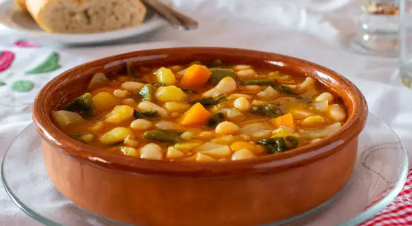 Un plato de barro con una sabrosa comida típica de Castellón: judías blancas, patatas, zanahoria y verduras en un caldo reconfortante.