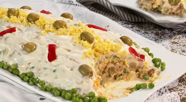 Ensaladilla rusa, receta de la abuela, cubierta de mayonesa, aceitunas, huevo rallado y pimientos.