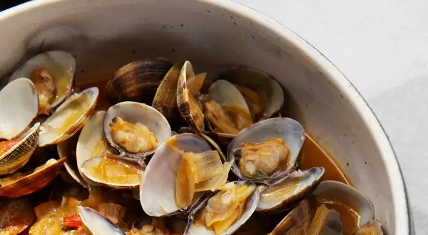 Un tazón lleno de almejas a la marinera, con sus conchas abiertas y jugosas, nadando en una salsa dorada.