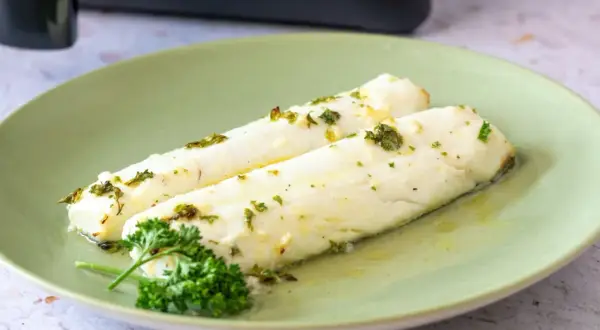 Dos filetes de merluza jugosa, recién hechos en airfryer, con hierbas frescas y aceite de oliva.