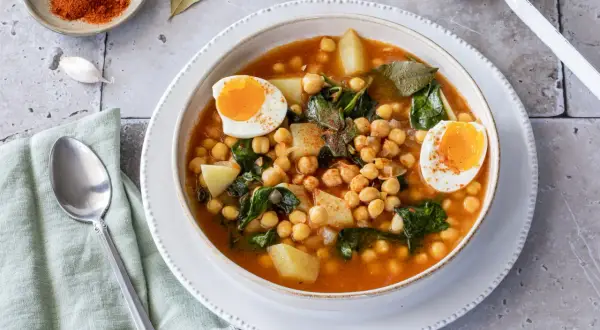 Un reconfortante plato de garbanzos con espinacas, patatas y huevos duros, espolvoreado con pimentón.