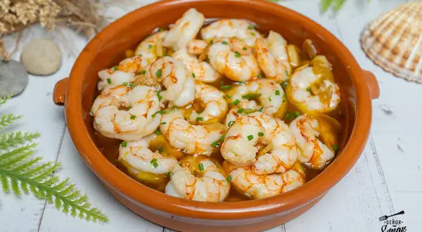 Un plato de gambas al ajillo burbujeantes en una cazuela de barro, adornado con perejil picado.