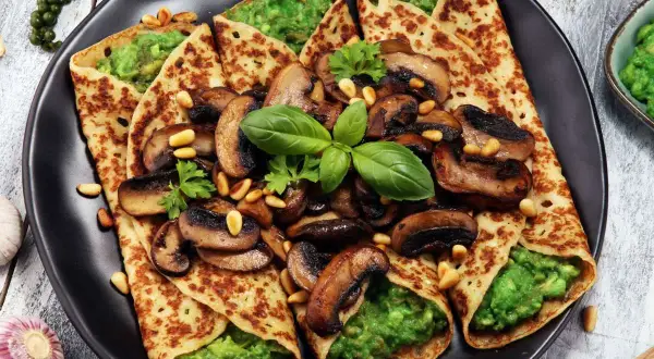 Crepes salados rellenos de aguacate y champiñones salteados, decorados con piñones y albahaca fresca.