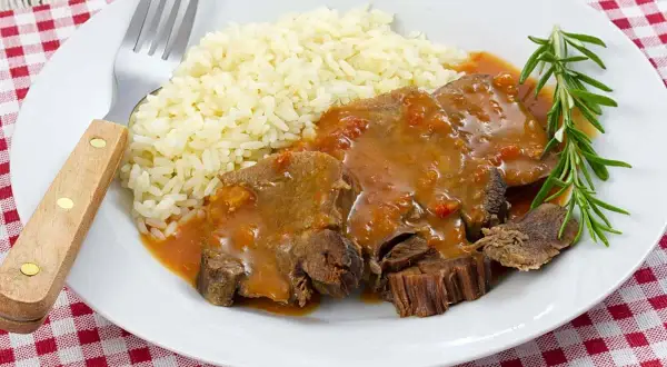Deliciosa lengua en salsa con arroz blanco y una ramita de romero. Un plato reconfortante listo para disfrutar.