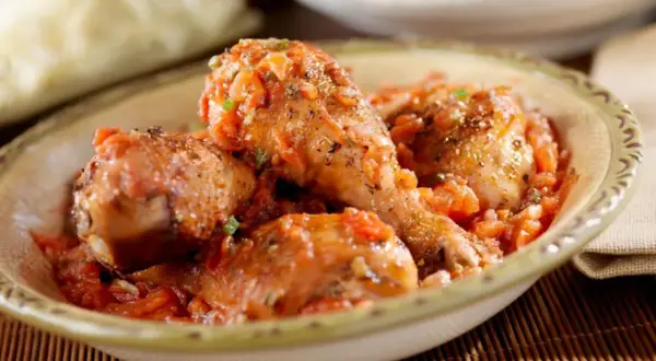 Sabroso pollo guisado en una salsa de tomate con hierbas, servido en un cuenco rústico.