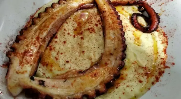 Tentáculos de pulpo a la plancha, dorados y tiernos, servidos sobre puré cremoso y espolvoreados con pimentón.