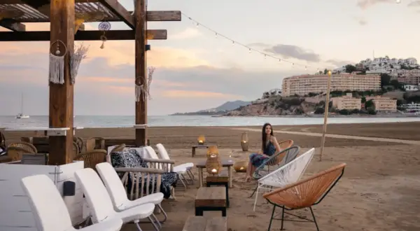 Una mujer disfruta de la tarde en la playa sur Peñíscola, sentada en una silla de diseño frente al mar.