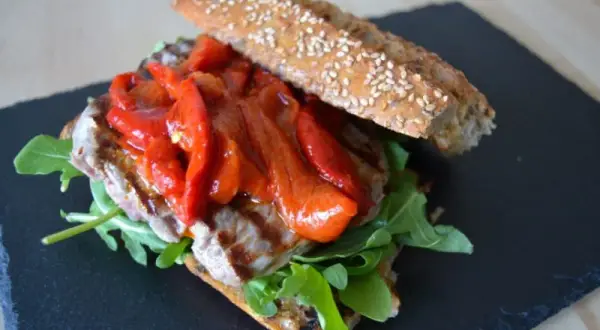 Un delicioso pepito de ternera con pimientos rojos asados y rúcula, servido en pan rústico con semillas.