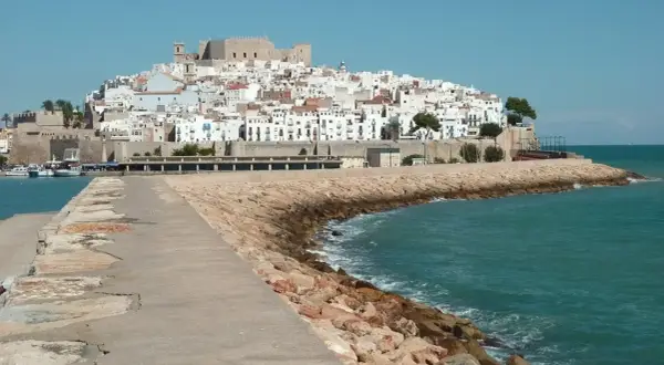 Pueblos costa Azahar: un castillo y casas blancas se alzan sobre una colina, con el mar turquesa y un rompeolas de rocas.