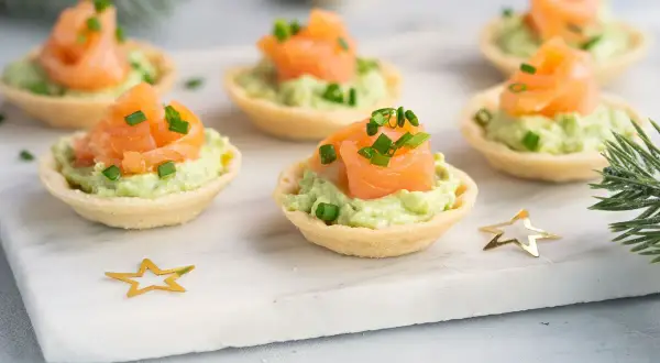 Aperitivos baratos para mucha gente: tartaletas crujientes con aguacate cremoso y salmón ahumado, decoradas con cebollino. ¡Perfectas para fiestas!