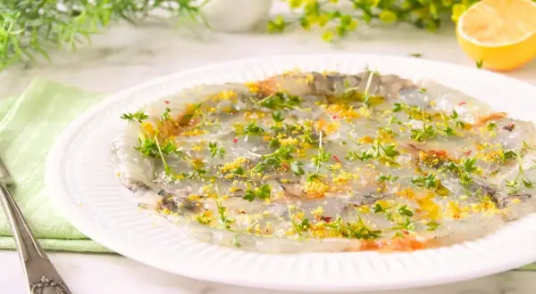 Delicado carpaccio de gambas con hierbas frescas y ralladura de limón, listo para disfrutar.