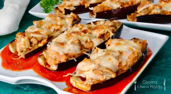 Berenjenas rellenas de atún gratinadas con queso, servidas sobre una base de salsa roja.