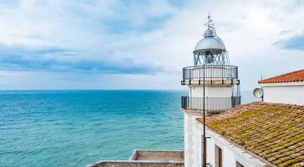 El faro de Peñíscola se alza vigilante sobre el mar turquesa, con un cielo nublado que promete aventura.