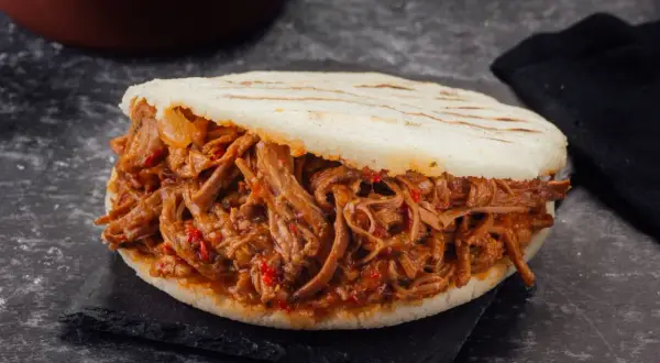 Arepa rellena de carne mechada jugosa y tierna, con trozos de pimiento rojo.