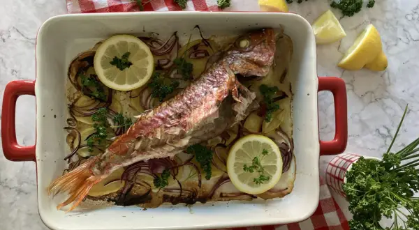 Deliciosos salmonetes al horno con patatas, cebolla roja, limón y perejil fresco, listos para servir.