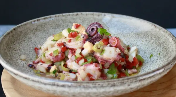 Salpicon de pulpo fresco con pimientos, cebolla y perejil, servido en un cuenco rústico.