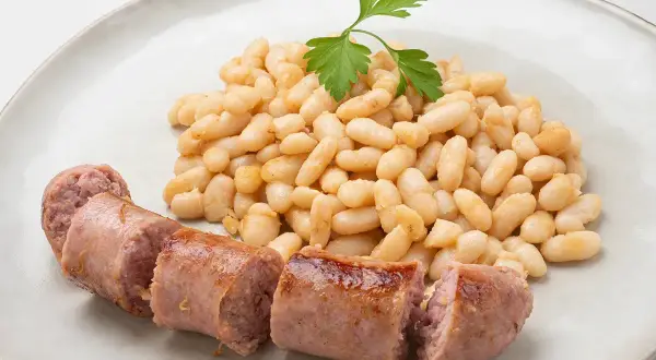 Un plato de alubias blancas tiernas y jugosas salchichas, decorado con una ramita de perejil fresco.