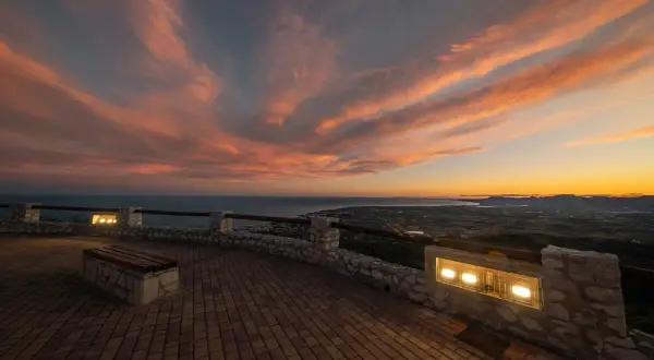 Atardecer espectacular sobre el mar y la costa. Un mirador perfecto para ver qué ver en Alcossebre, con un banco y luces que invitan a contemplar.