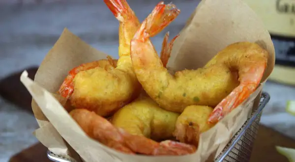 Crujientes gambas a la gabardina doradas y jugosas, servidas en una cesta metálica con papel de estraza.
