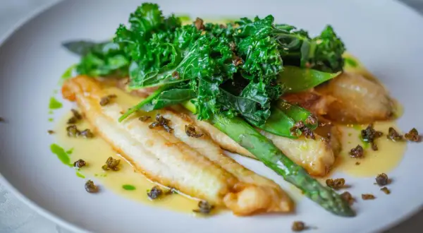 Filetes de bacalao en salsa verde, acompañados de espárragos y kale crujiente.