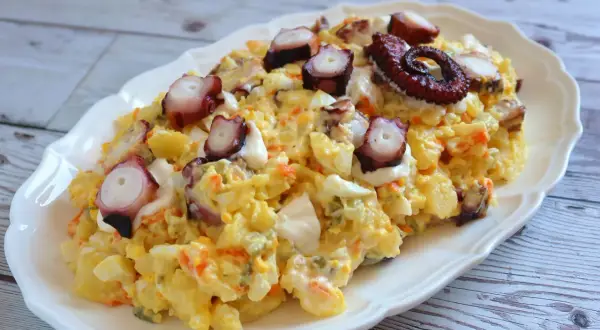 Deliciosa ensaladilla de pulpo con patatas, huevo y zanahoria, coronada con trozos de pulpo tierno y un toque de mayonesa.