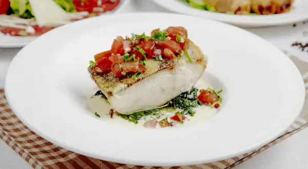 Filete de bacalao con tomate y hierbas, sobre espinacas y salsa cremosa. Un plato principal ideal para tus recetas de bacalao.