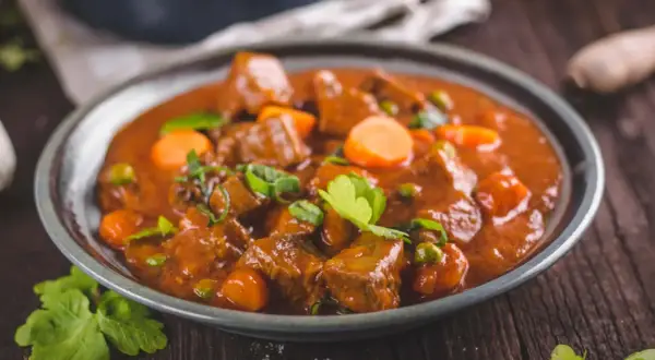 Un plato humeante de rabo de ternera estofado con zanahorias y guisantes, adornado con perejil fresco.