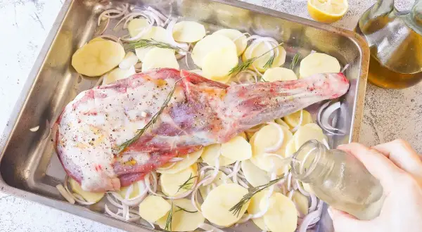 Paletilla de cordero al horno lista para asar con patatas, cebolla y romero. Un chorrito de aceite y al horno.