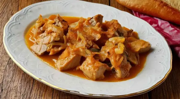 Sabroso atún encebollado en una salsa dorada, servido en un plato blanco con borde dorado.