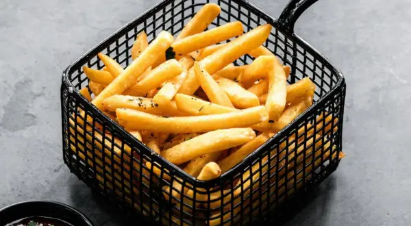 Patatas soufflé doradas y crujientes en una cesta negra, listas para ser disfrutadas con una salsa.